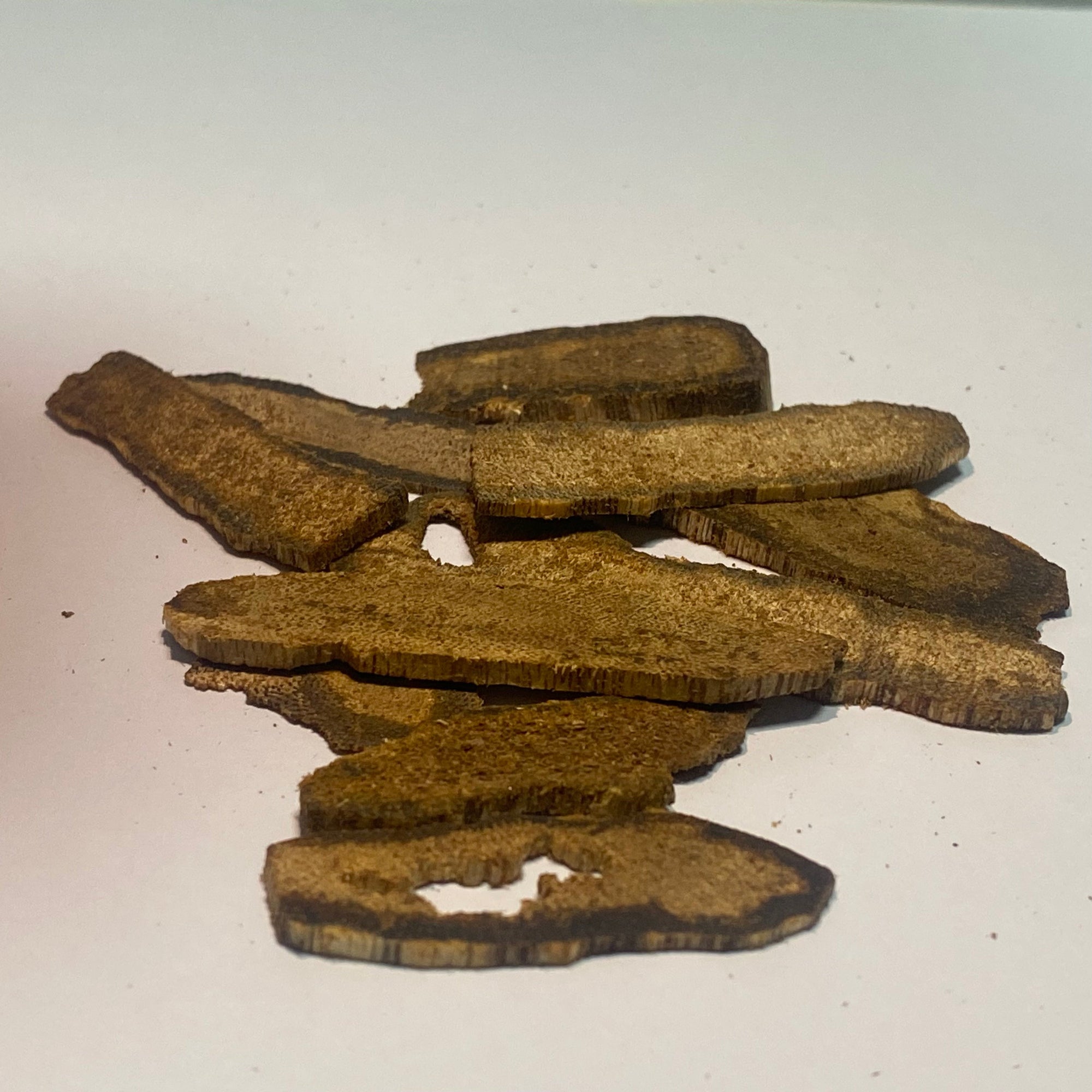 Pile of dark resinous agarwood chips with rich oil veins on a white surface