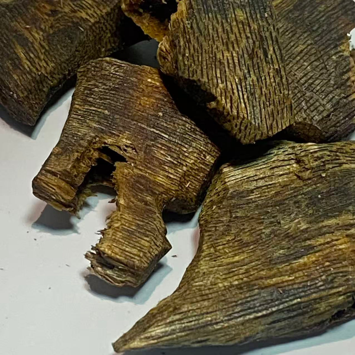 Oily dark oud wood chunks in close-up against a plain white surface