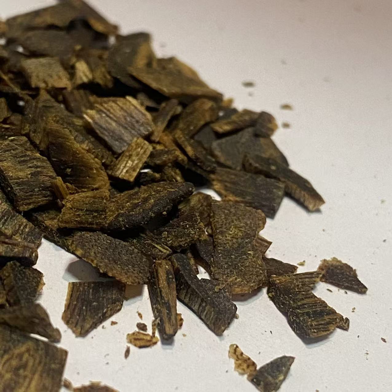 Small crushed oud wood chips scattered across a clean white background
