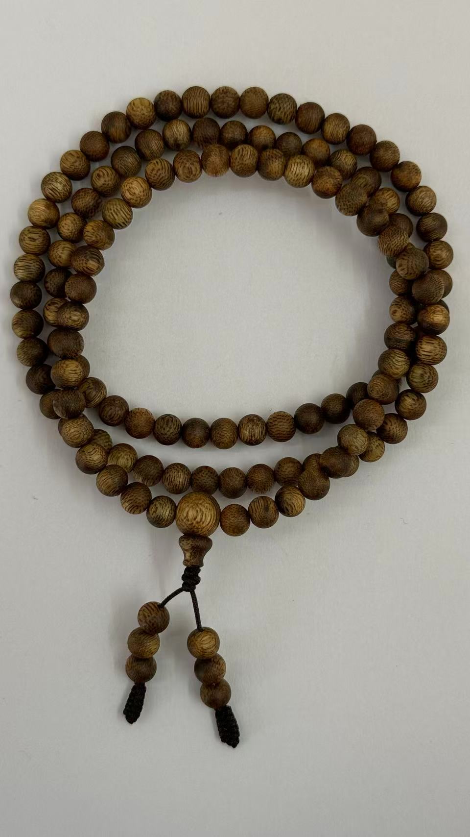 Agarwood mala necklace with guru bead and tassel coiled on white paper