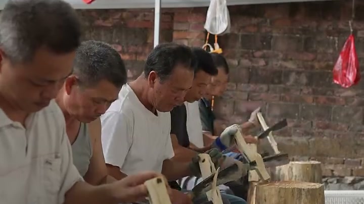 Workers carving agarwood chips by hand with hook knives at a Dianbai processing workshop